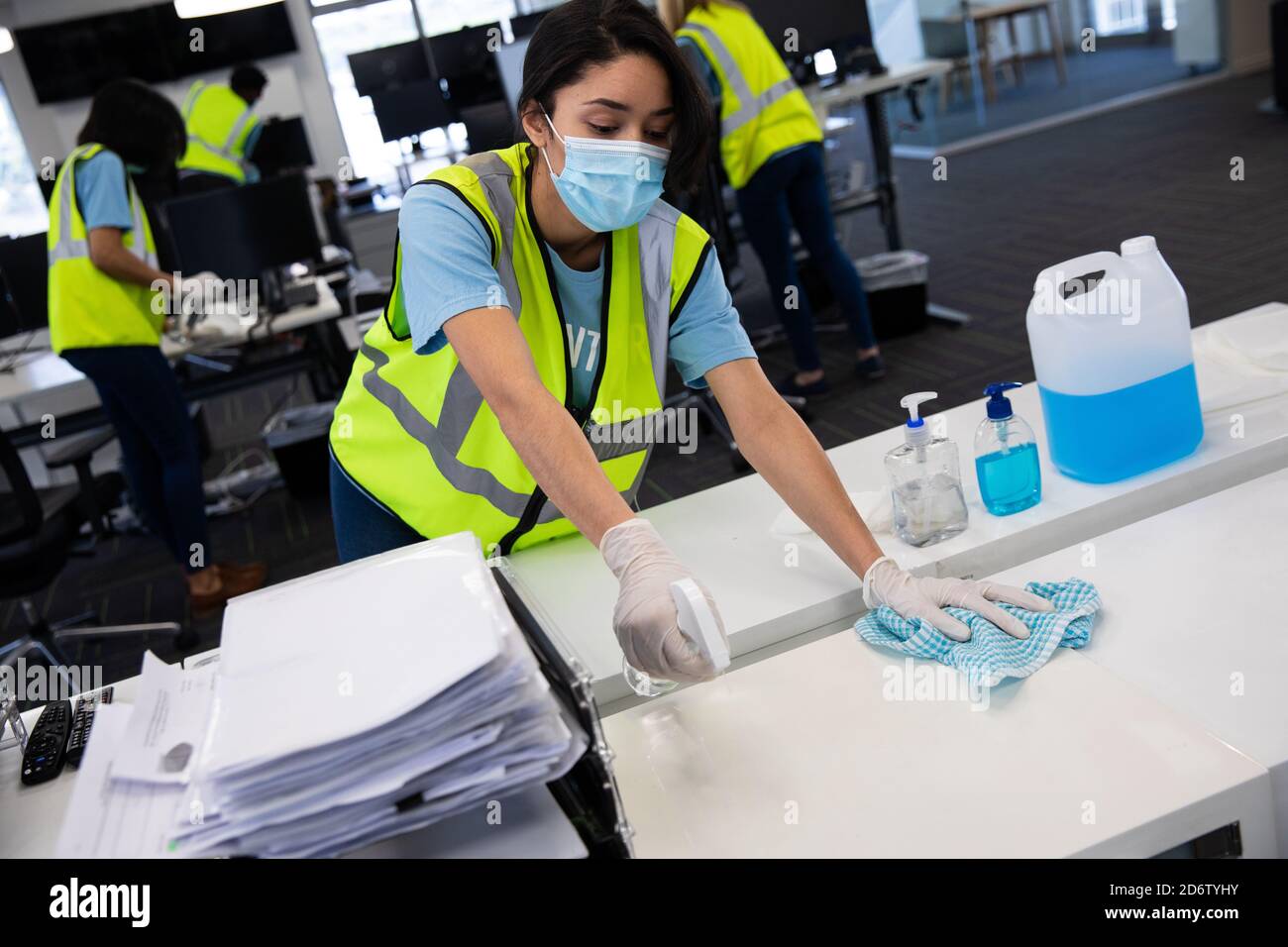 Femme portant un gilet haute visibilité et un masque de nettoyage du bureau utilisant du désinfectant Banque D'Images