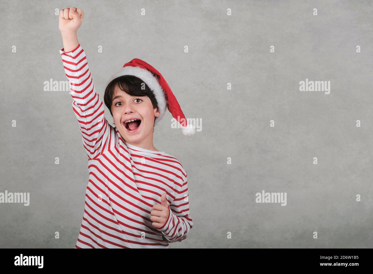 Joyeux Noël, jeune enfant souriant portant le chapeau du Père Noël sur fond gris Banque D'Images