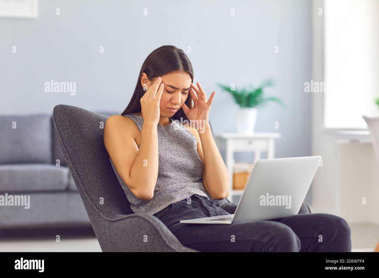 Jeune femme fatiguée frottant des temples souffrant de maux de tête assis dans fauteuil avec ordinateur portable à la maison Banque D'Images