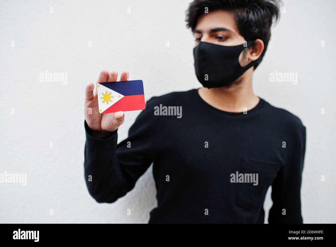 Homme asiatique porter tout noir avec masque de visage tenir drapeau des Philippines à la main isolé sur fond blanc. Concept de pays du coronavirus. Banque D'Images