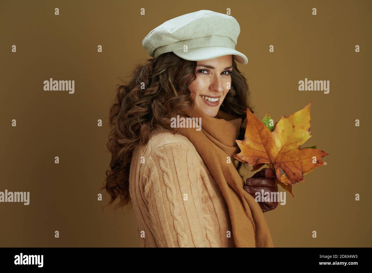 Bonjour novembre. Portrait d'une femme heureuse d'âge moyen en foulard avec gants en cuir et feuilles d'érable jaune d'automne isolées sur beige. Banque D'Images