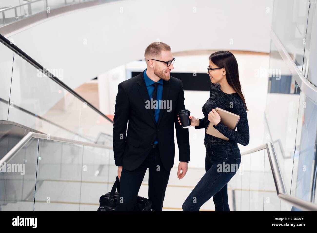 Belle femme d'affaires et homme leur tenant une tablette dans les mains et parlant les uns avec les autres tout en se tenant à l'escalier dans le bâtiment de bureau moderne. Banque D'Images