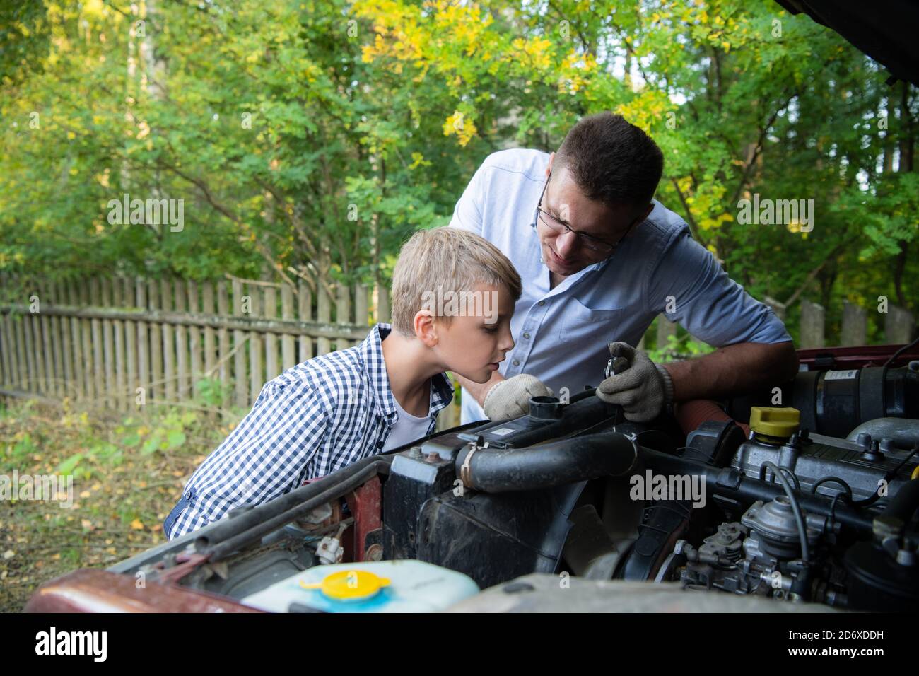 Papa et son fils réparent la voiture avec le capot ouvert à l'extérieur, fixant le moteur Banque D'Images