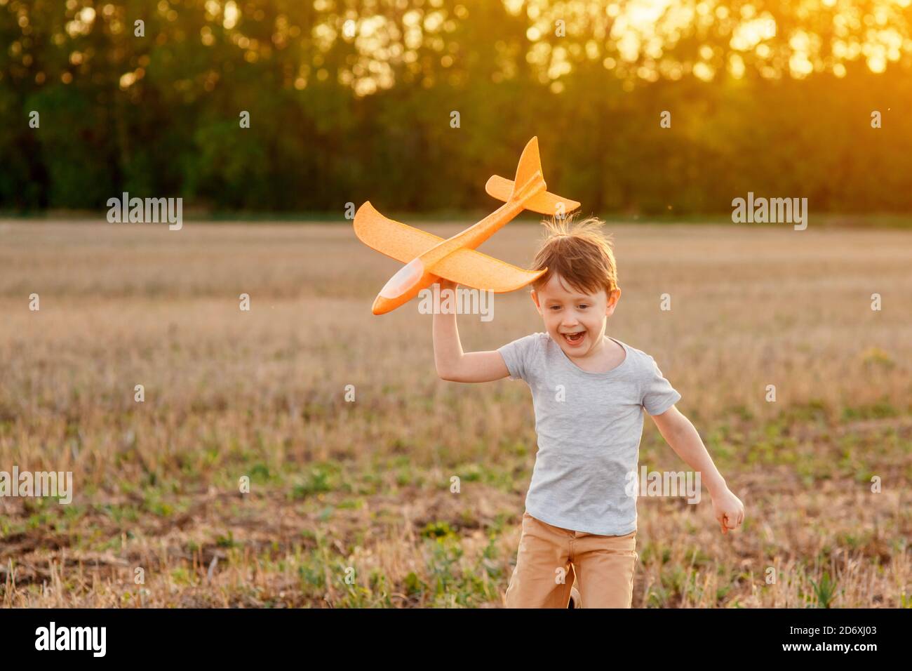 Un enfant heureux court avec un avion jouet sur un fond de coucher de soleil sur un champ. Le concept d'une famille heureuse. Rêves d'enfance Banque D'Images