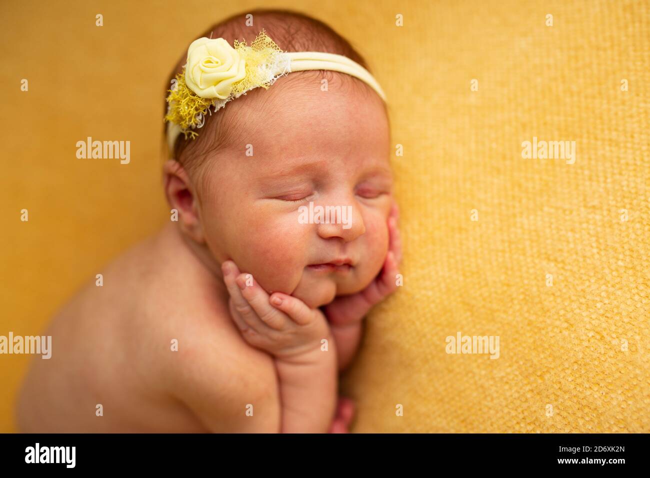 portrait d'une belle jeune fille de neuf jours dormant dans une position de ftal enroulée sur une couverture jaune. Elle porte un bandeau rose jaune Banque D'Images