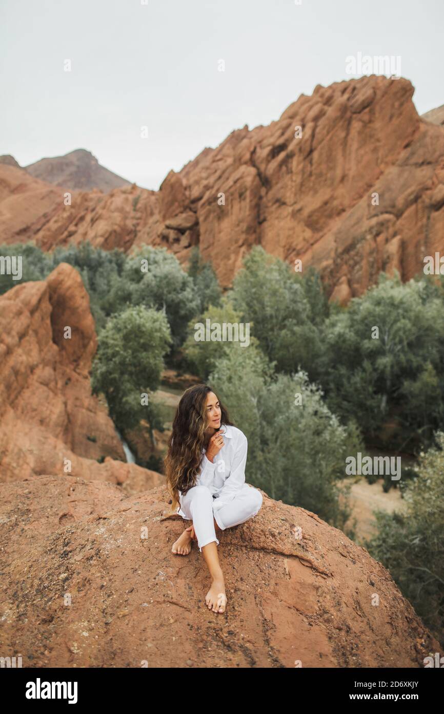 Jolie femme brune blanche assise et vue sur le canyon de la gorge de Todra au Maroc. Harmonie avec la nature et la liberté. Style de vie de voyage. Banque D'Images