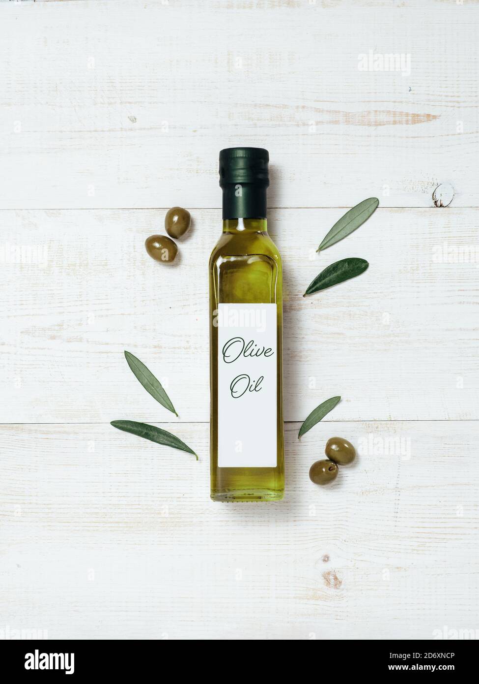 Maquette de bouteille en verre à l'huile d'olive. Vue de dessus d'une bouteille en verre vert avec de l'huile d'olive extra vierge sur fond de bois blanc avec des olives vertes et des feuilles d'oliviers verts frais. Verticale. Copier l'espace. Banque D'Images
