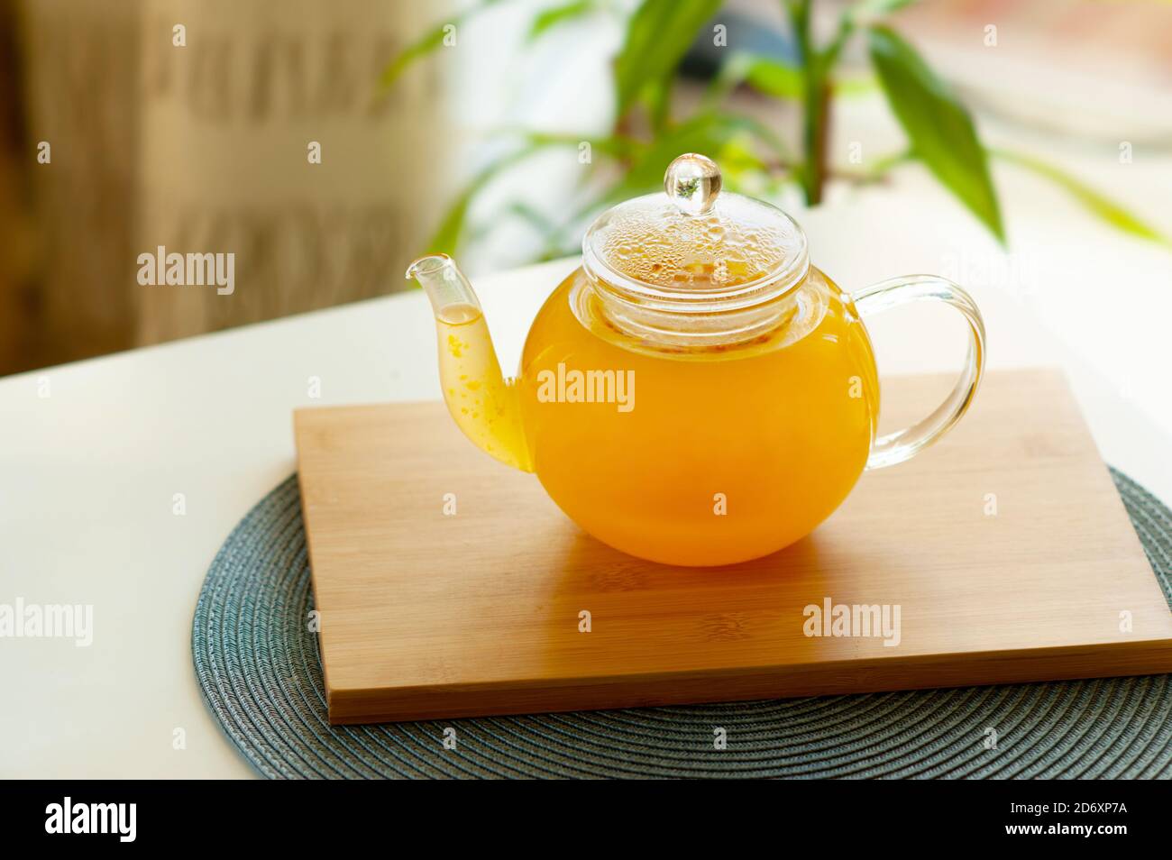 thé de vitamine aux baies d'argousier dans une théière élégante en verre transparent avec un long bec sur un support en bois sur un fond flou de l'intérieur, sel Banque D'Images