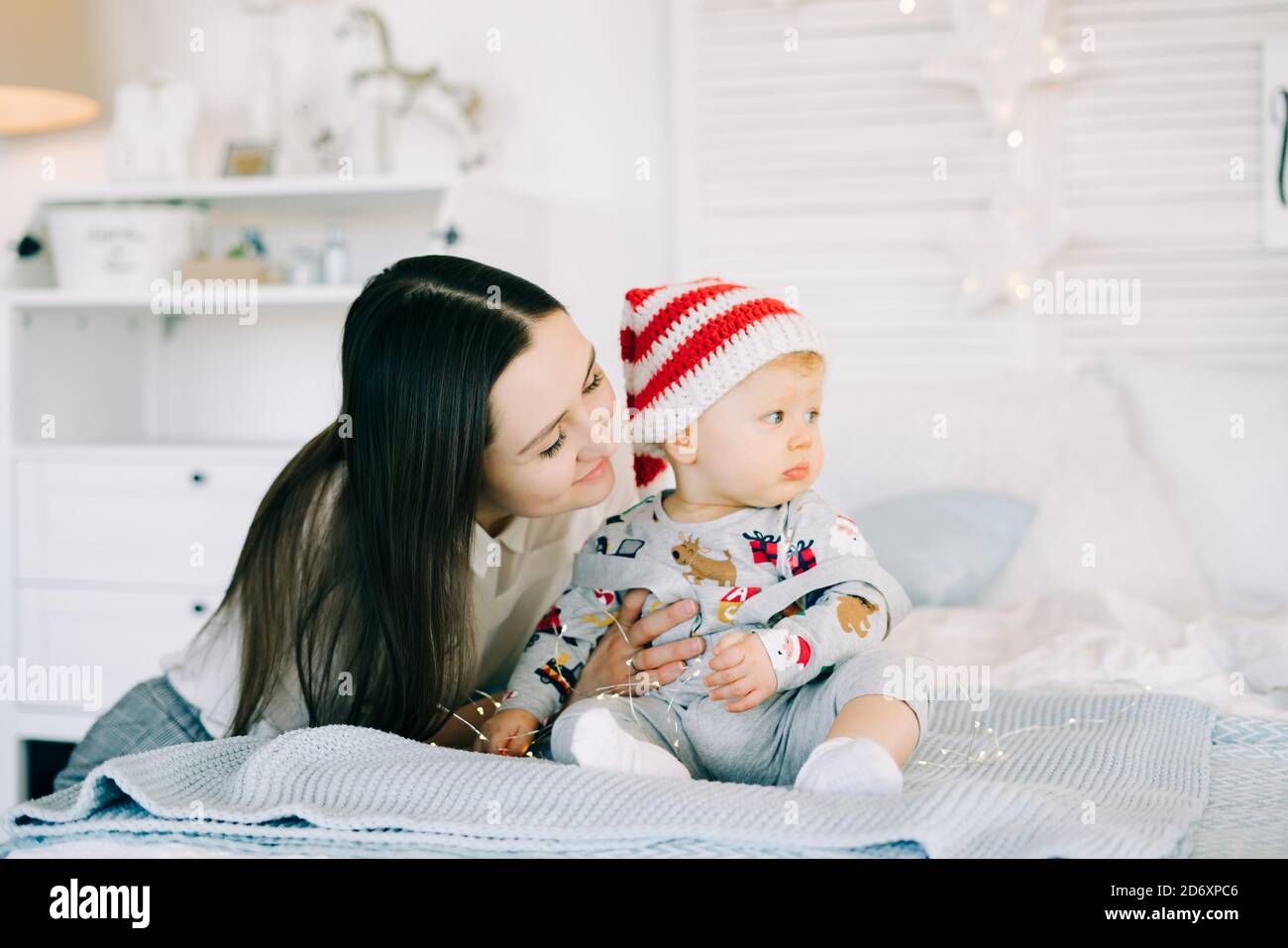 Le premier Noël de l'enfant. Petit garçon mignon dans un chapeau de Père Noël, assis sur le lit avec son concept de Noël de mère. Banque D'Images