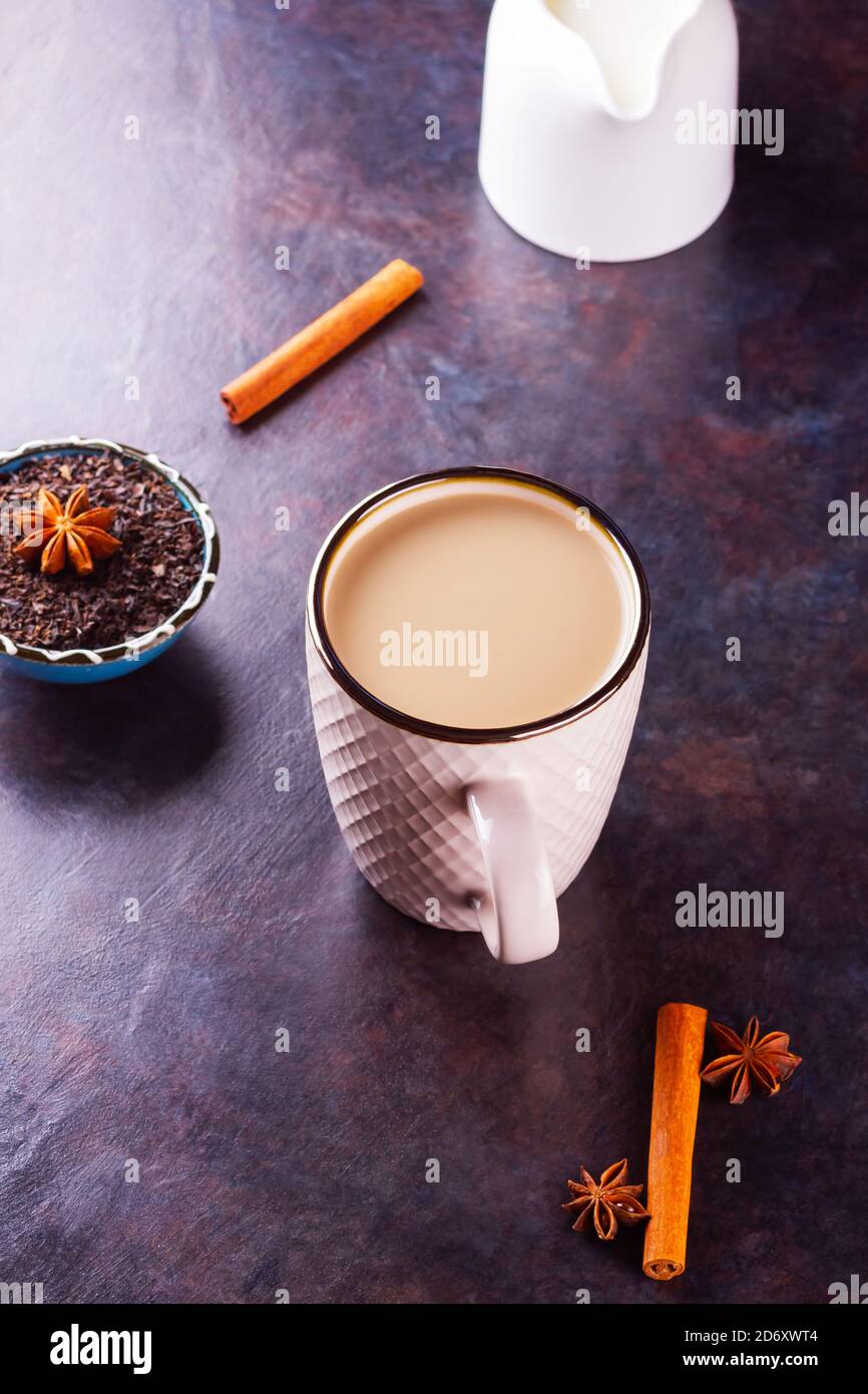 Thé Chai de masala. Boisson traditionnelle indienne - thé masala avec épices sur fond sombre. Tasse d'épices en céramique, thé et pot à lait blanc Banque D'Images
