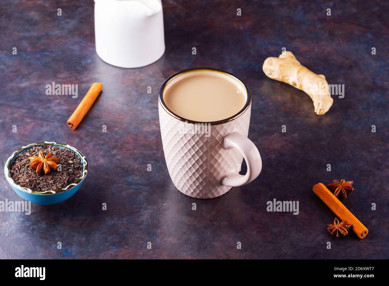 Thé Chai de masala. Boisson traditionnelle indienne - thé masala avec épices sur fond sombre. Tasse d'épices en céramique, thé et pot à lait blanc Banque D'Images