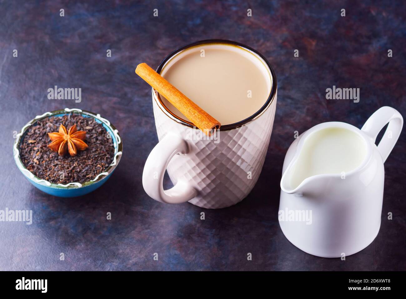 Thé Chai de masala. Boisson traditionnelle indienne - thé masala avec épices sur fond sombre. Tasse d'épices en céramique, thé et pot à lait blanc Banque D'Images