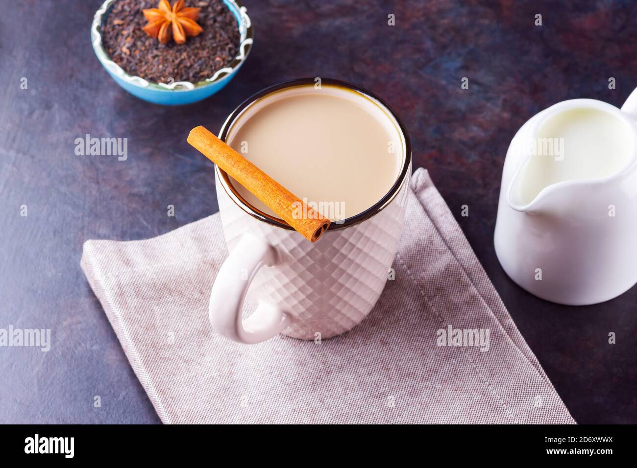 Thé Chai de masala. Boisson traditionnelle indienne - thé masala avec épices sur fond sombre. Tasse d'épices en céramique, thé et pot à lait blanc Banque D'Images