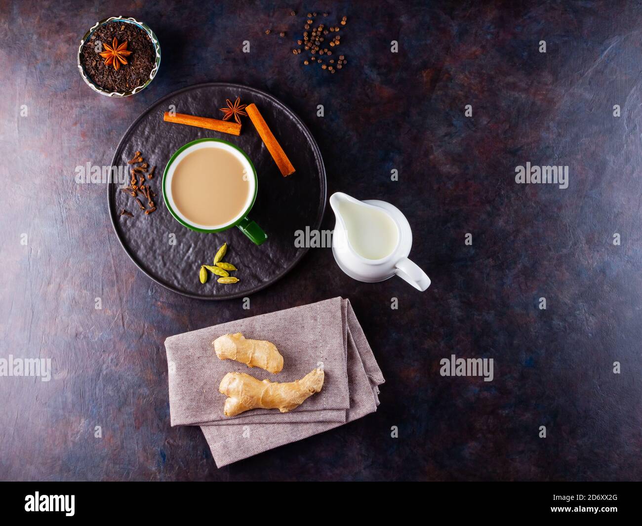 Thé Chai de masala. Boisson traditionnelle indienne - thé masala avec diverses épices sur une assiette noire. Tasse d'épices en céramique, thé et pot à lait Banque D'Images