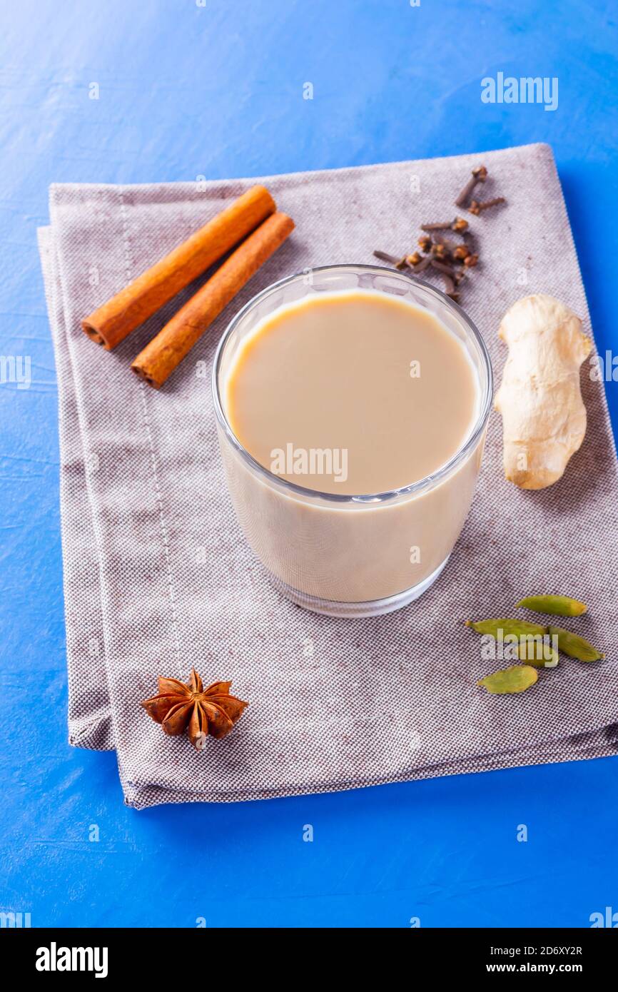 Thé au chaï masala sur une serviette en lin. Boisson traditionnelle indienne - thé masala avec diverses épices. Verre de thé masala sur fond bleu Banque D'Images