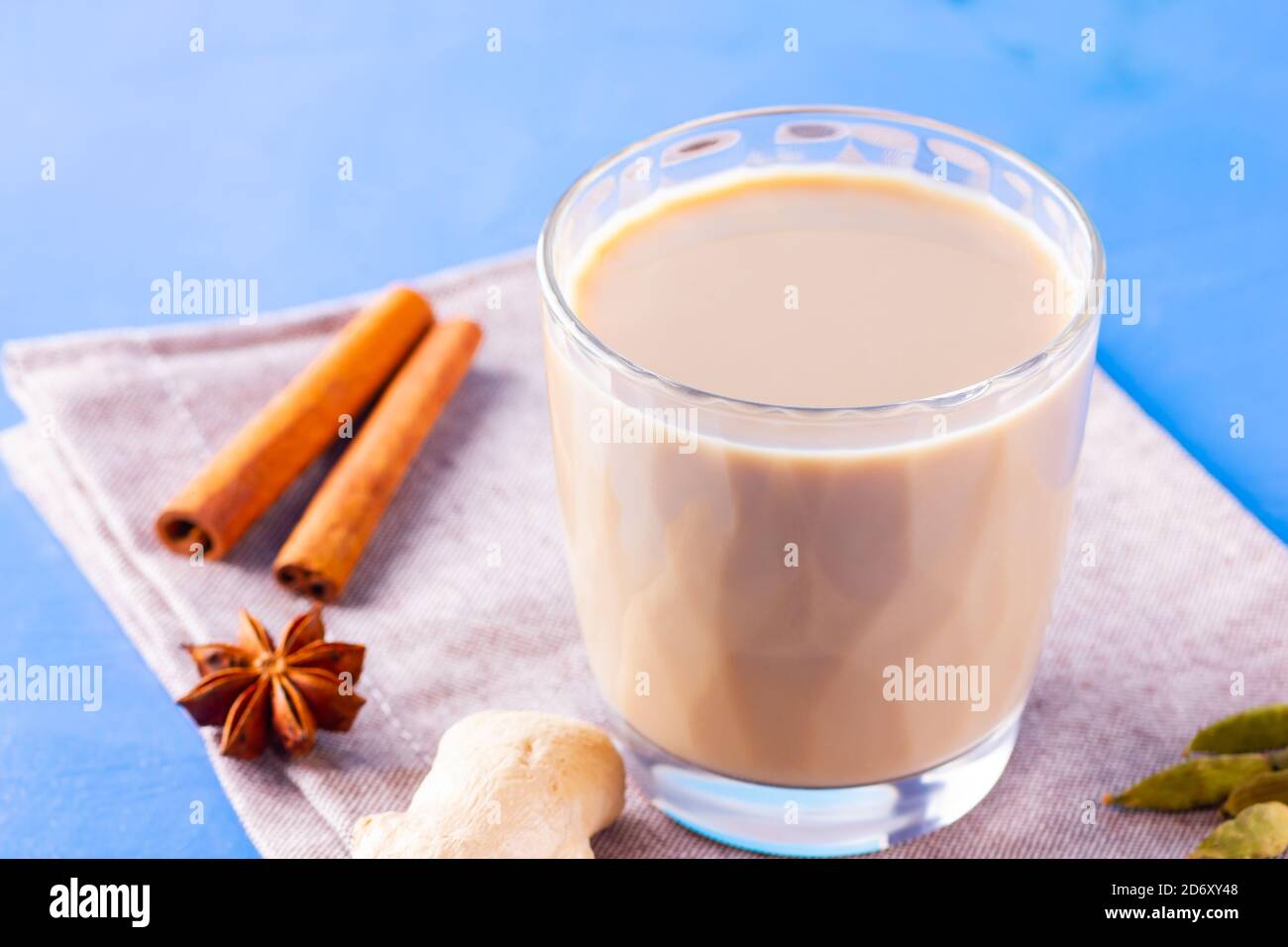 Thé au chaï masala sur une serviette en lin. Boisson traditionnelle indienne - thé masala avec diverses épices. Verre de thé masala sur fond bleu Banque D'Images