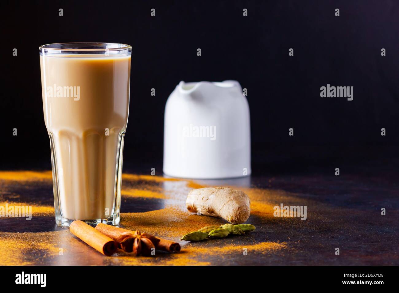Verre de thé masala et épices éparses. Masala chai thé et pot à lait sur fond noir. Copier l'espace Banque D'Images