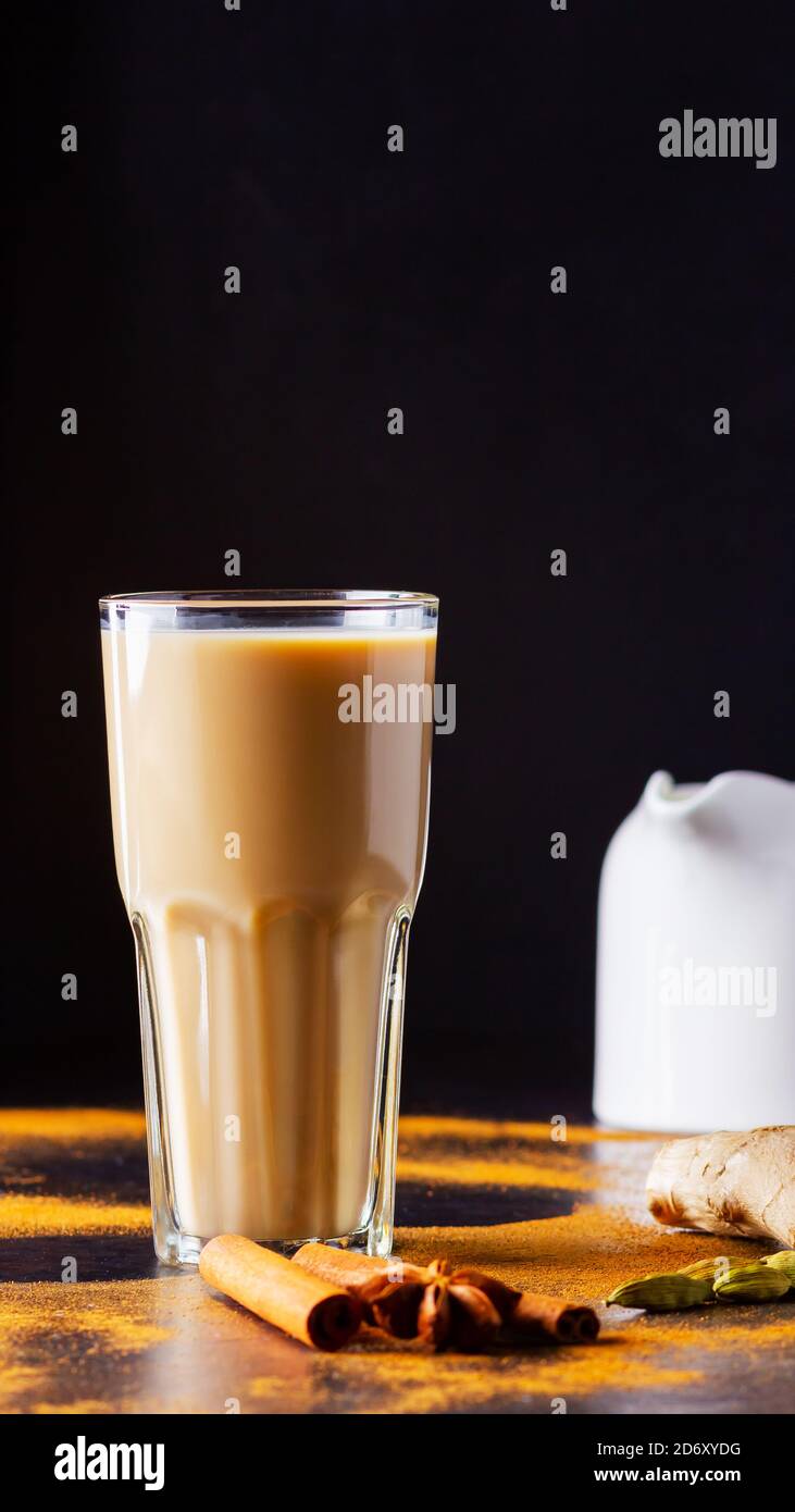 Verre de thé masala et épices éparses. Masala chai thé et pot à lait sur fond noir. Copier l'espace Banque D'Images