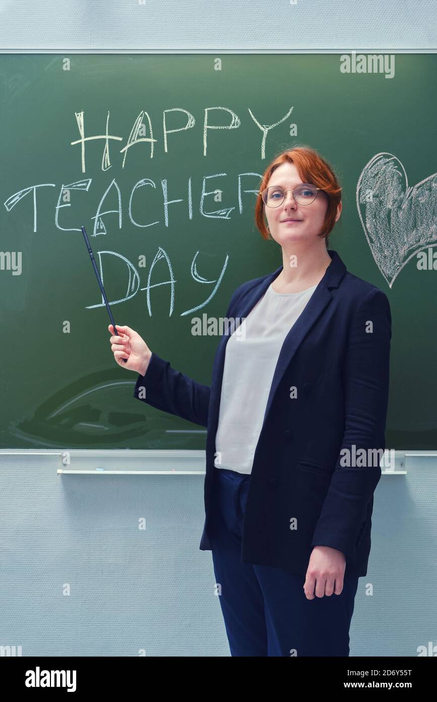 Bonne femme souriante debout à côté d'un tableau noir de l'école quel est le message d'accueil du professeur Banque D'Images