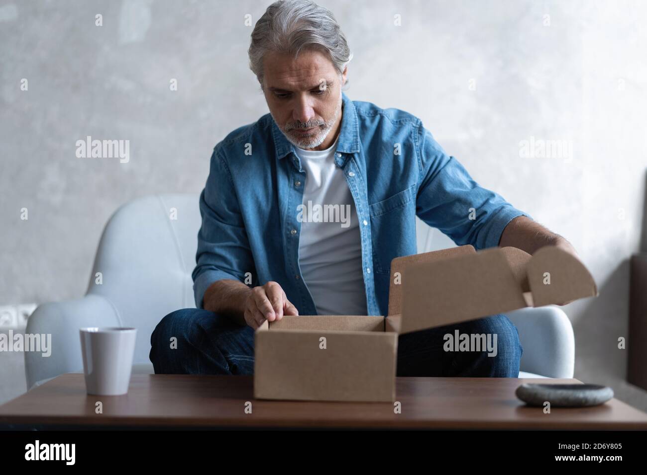 Sourire homme consommateur ouvrir boîte carton obtenir colis postal, client mâle recevoir paquet de carton s'asseoir sur le canapé à la maison Banque D'Images