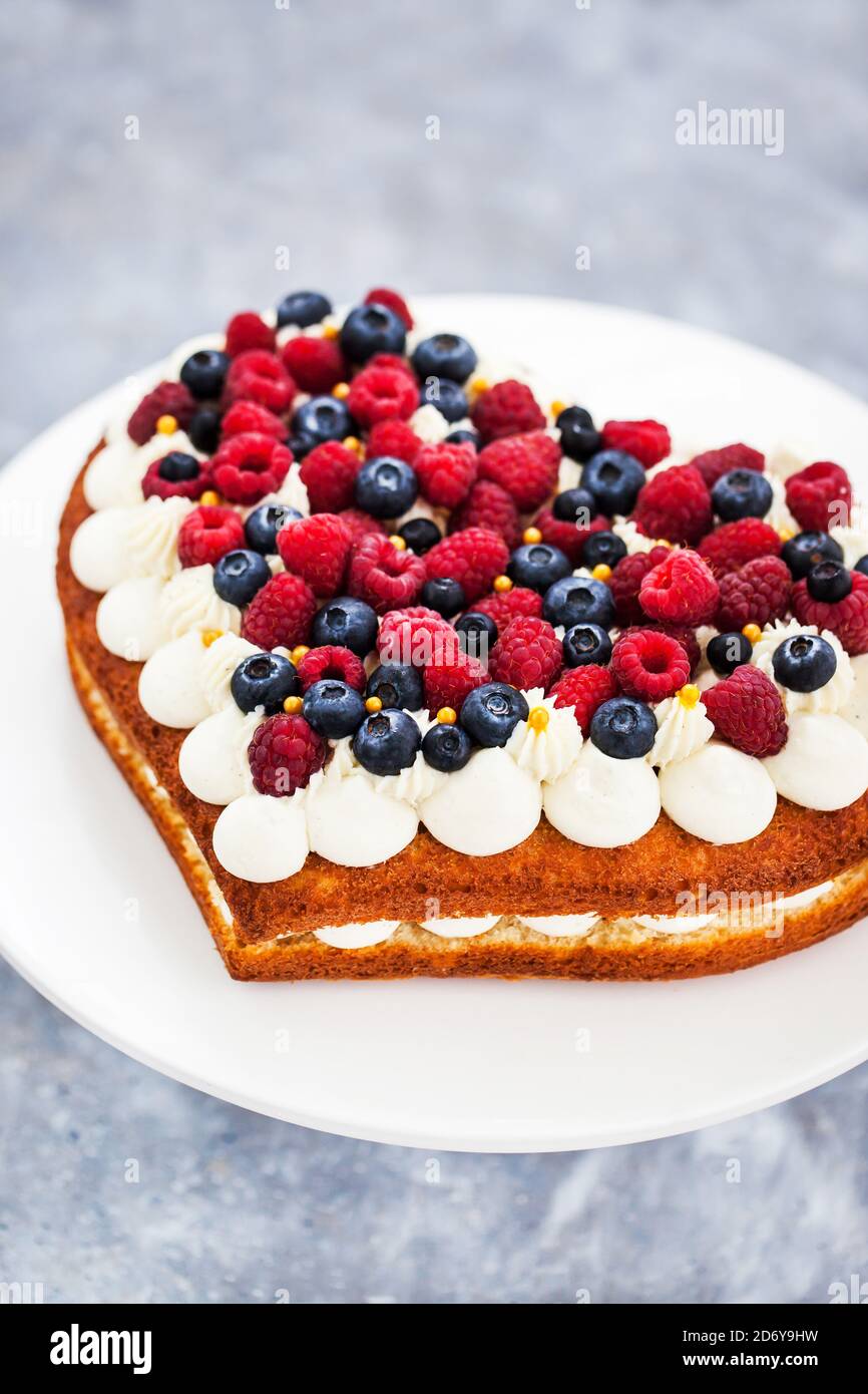 Délicieux gâteau à la vanille fait maison en forme de coeur décoré de crème et baies fraîches Banque D'Images