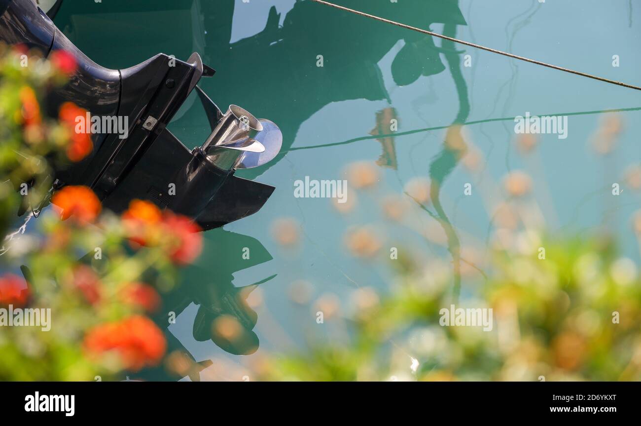 Une hélice en argent sur un moteur noir encadré de fleurs rouges et blanches, soulevées hors de l'eau, reflétée sur les eaux turquoises de la mer Ionienne. Banque D'Images