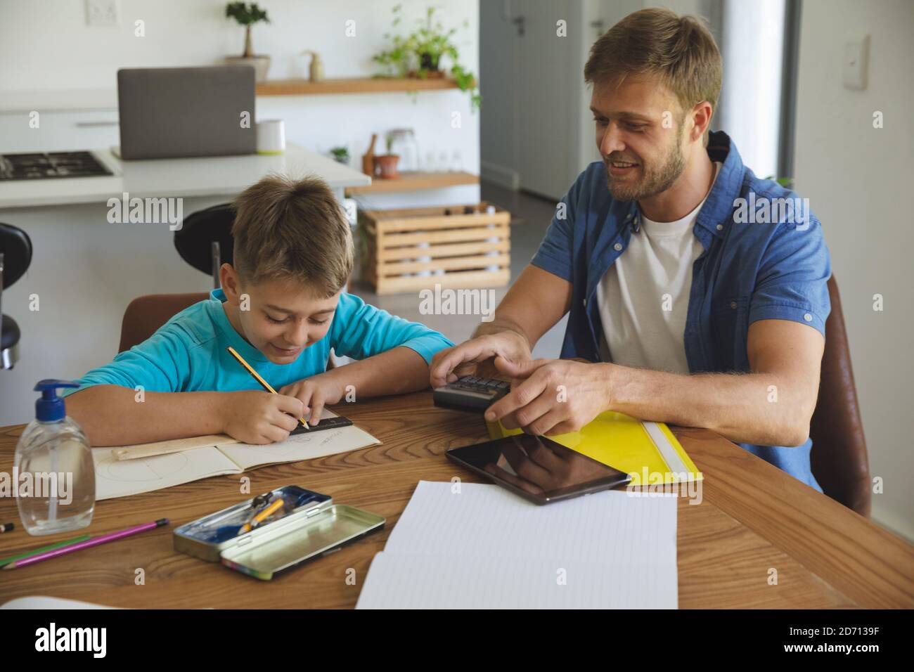 Homme caucasien à la maison avec son fils ensemble, en cuisine, père aidant le garçon faisant des devoirs à table. Distanciation sociale pendant le coronavirus Covid 19 Banque D'Images