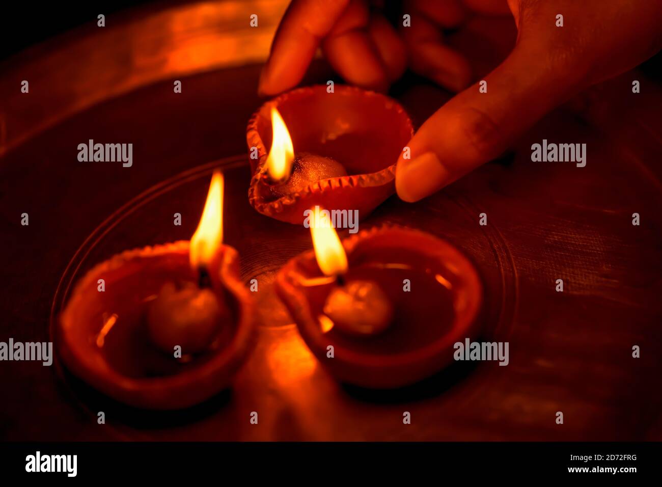Femme ou fille indienne tenant une diya d'argile éclairée dans sa main et éclairant d'autres lampes à huile avec elle dans un thali ou une assiette. Hindou Festival Diwali rituels. Banque D'Images
