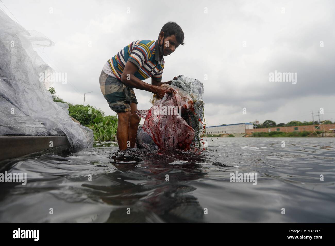 Un homme bangladais lave les déchets de plastique, qui ont été utilisés pour transporter des produits chimiques, dans l'eau de la rivière Turag avant de les recycler, à Tongi, près de Dhaka, Banque D'Images