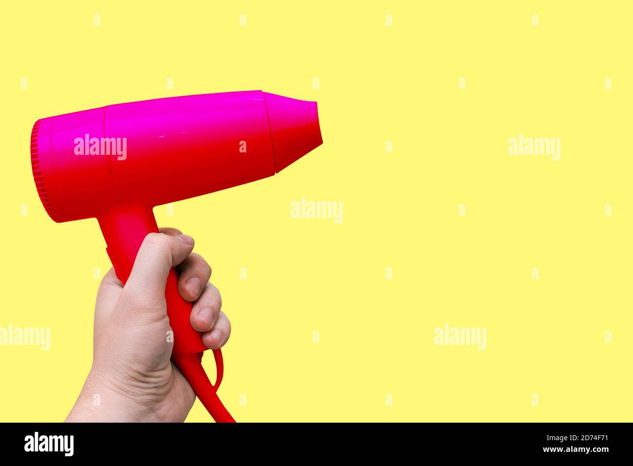 Sèche-cheveux électrique rouge dans les mains d'un homme, isolé sur fond jaune avec une copie de l'espace. Appareil moderne pour le séchage, le coiffage et la découpe Banque D'Images