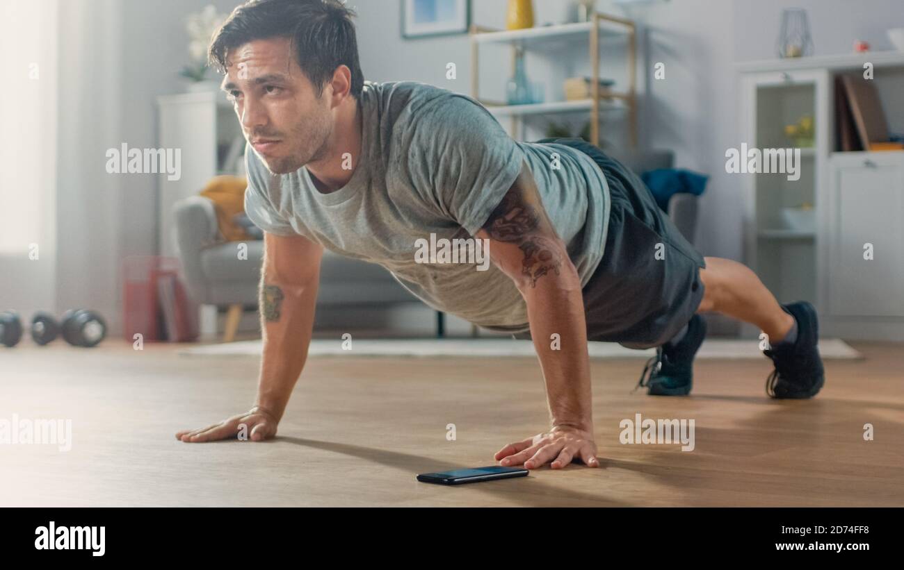 Athletic Fit Man en T-shirt et short fait des exercices push-up tout en utilisant un chronomètre sur son téléphone. Il est formation à la maison dans son salon avec Banque D'Images