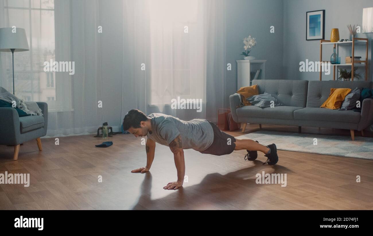 Muscle Athletic Fit Man en T-shirt et short fait des exercices push-up à la maison dans son salon spacieux et ensoleillé avec intérieur moderne. Banque D'Images