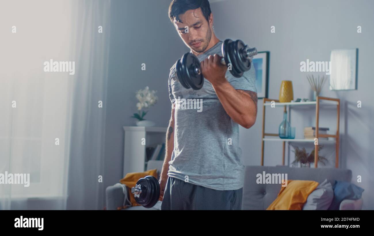 Un homme puissant et athlétique en T-shirt et en short est en train de faire Exercices d'élévation de veau avec haltères à la maison dans son spacieux Et lumineux appartement avec Banque D'Images