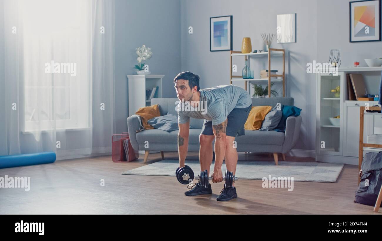 Muscle Athletic Fit Man dans le tee-shirt et le short fait Exercices avec haltères à la maison dans son spacieux et lumineux Séjour avec minimalistes Banque D'Images