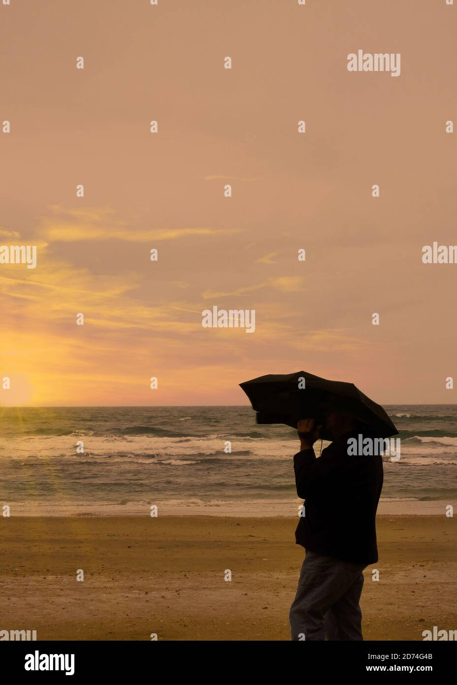 Silhouette de la personne sur la plage tenant un parasol Banque D'Images