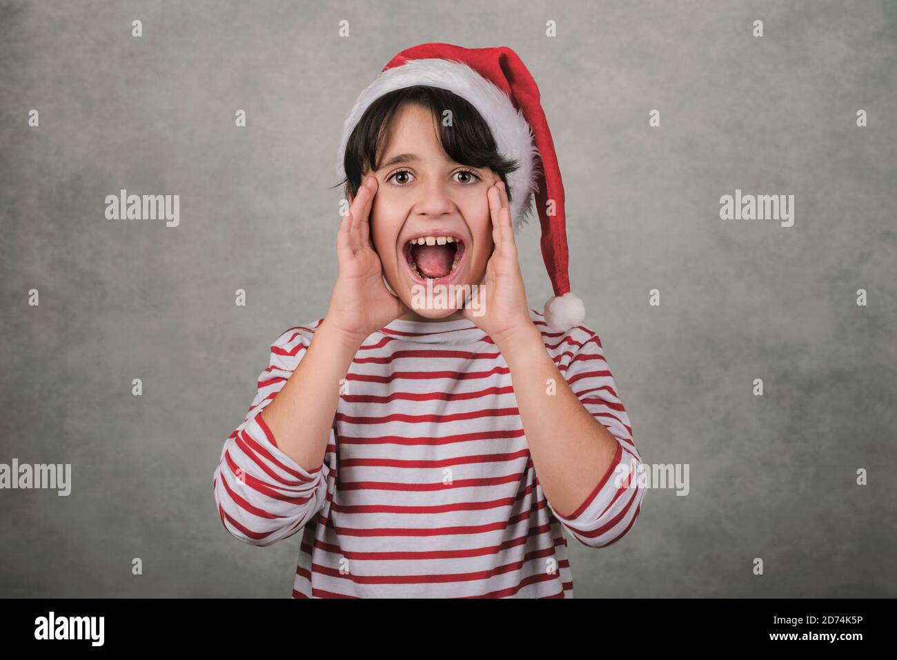 Joyeux Noël, gamin hurlant portant le chapeau du Père Noël sur fond gris Banque D'Images