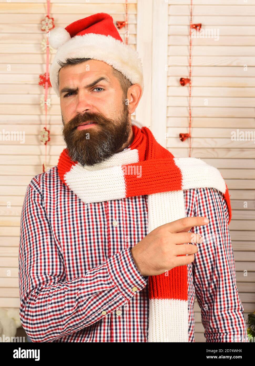 Concept de mode célébration et nouvel an. Homme avec barbe en chemise à  carreaux. Guy en chapeau règle le foulard rouge et blanc. Le Père Noël avec  une face stricte sur un
