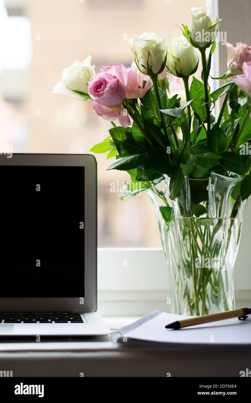Beau bureau à la maison avec des roses et un ordinateur portable pour travailler de accueil par la fenêtre Banque D'Images
