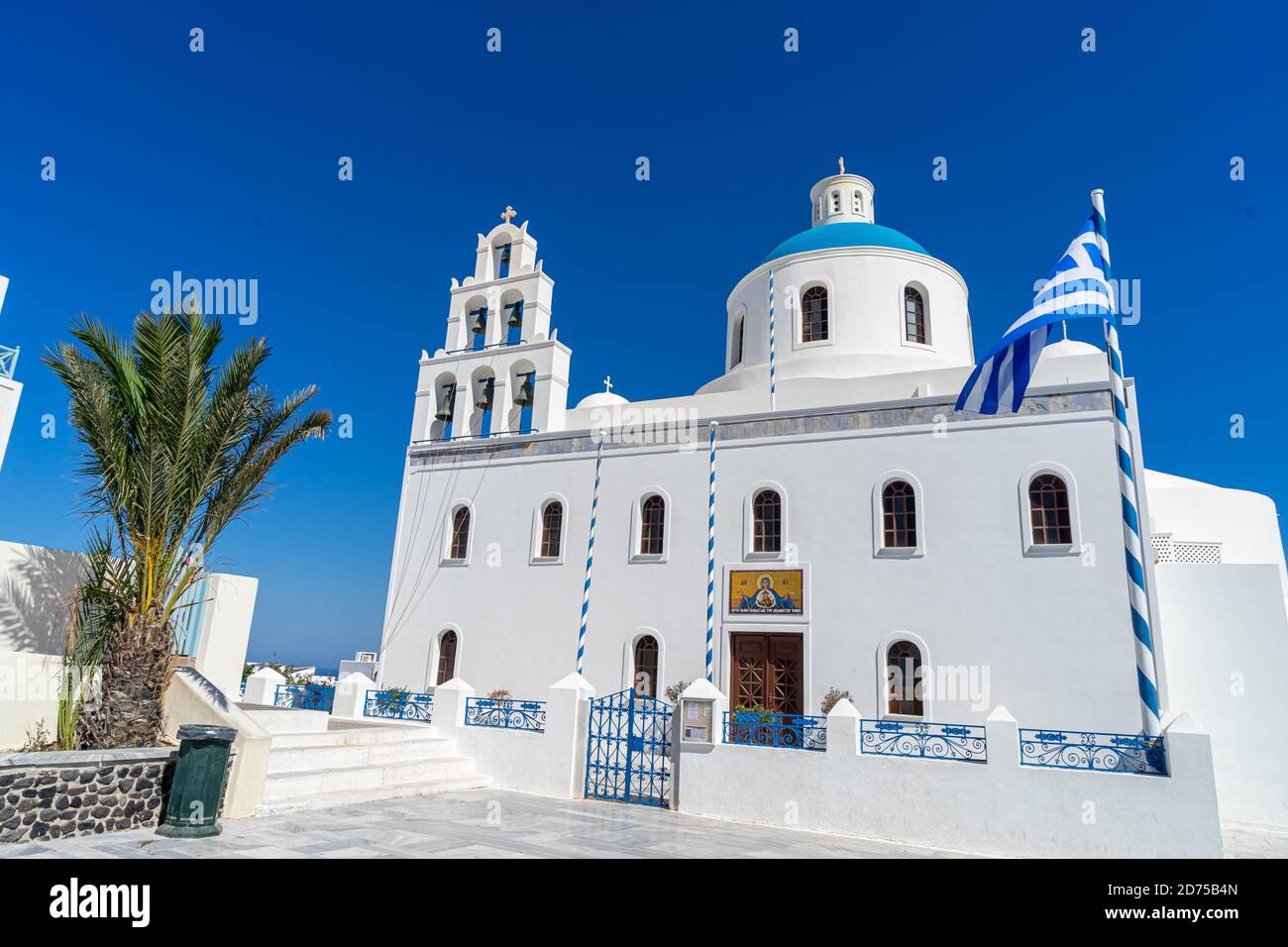 Eglise orthodoxe à Oia, Santorin, Grèce, un jour d'été avec drapeau grec. Beau ciel bleu clair. Banque D'Images