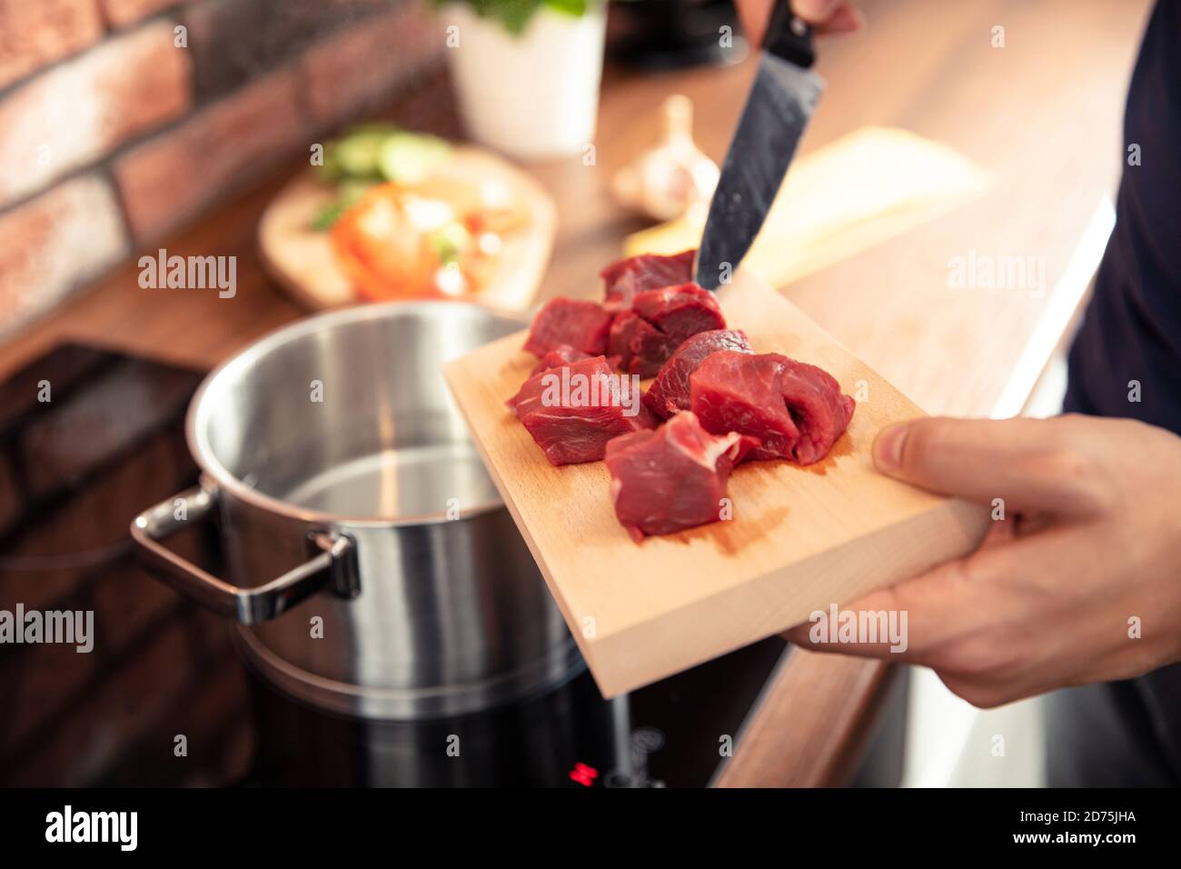 La main de l'homme dépose la viande fraîchement coupée dans un pot de eau Banque D'Images