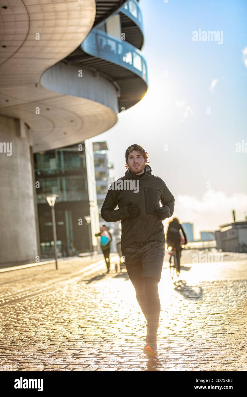 Hiver homme de course à pied portant froid hiver vêtements d'extérieur vêtements d'entraînement extérieur. Homme athlète ville jogging urbain à l'extérieur sur la rue Europe Banque D'Images