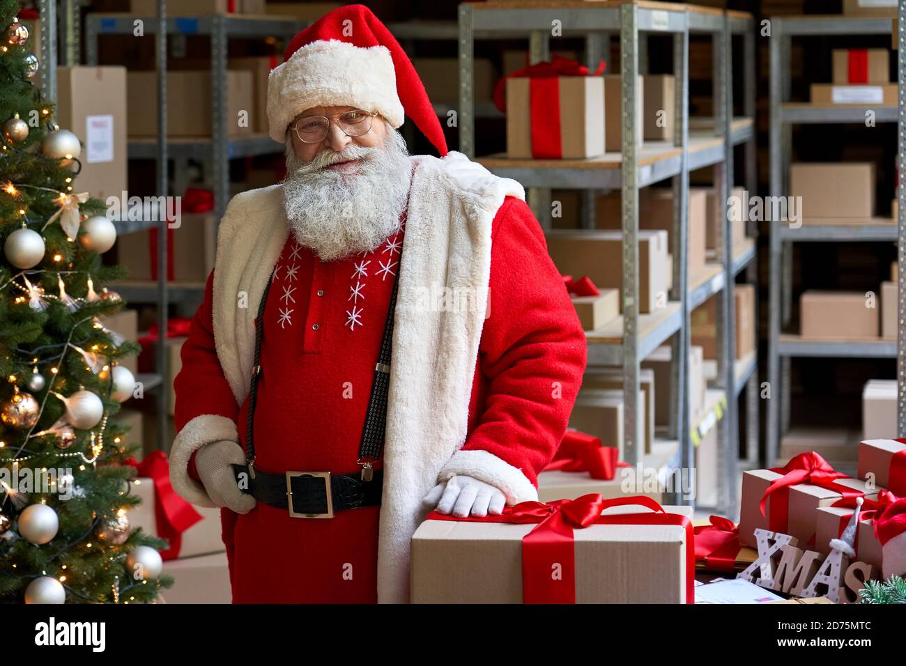 Joyeux Père Noël portant un costume posant en atelier avec des cadeaux, portrait. Banque D'Images
