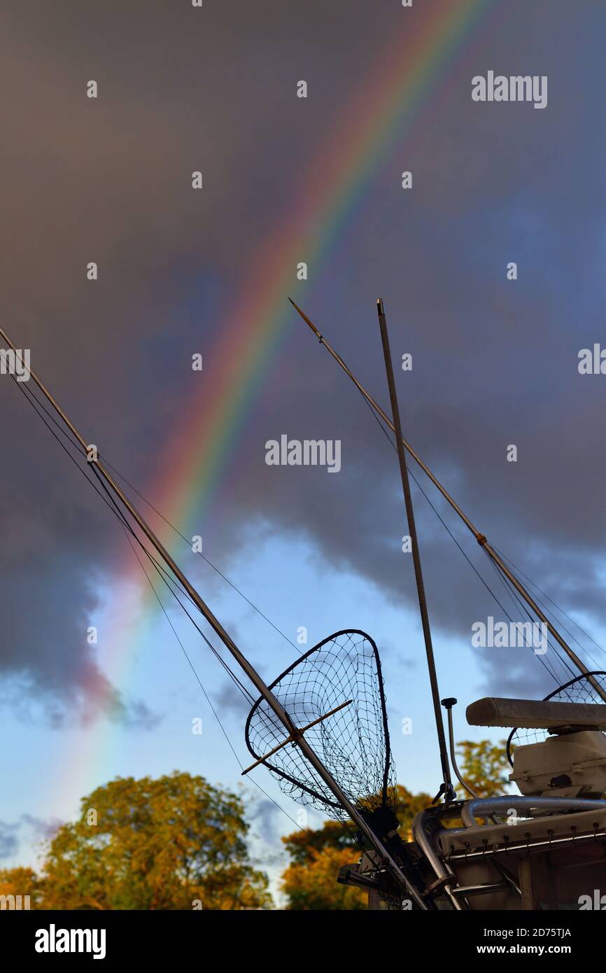Saugatuck, Michigan, États-Unis. Des bâtons de pêche et un filet à bord d'un bateau fournissent un premier plan à un arc-en-ciel alors que le soleil de la fin de l'après-midi émerge des nuages de tempête. Banque D'Images