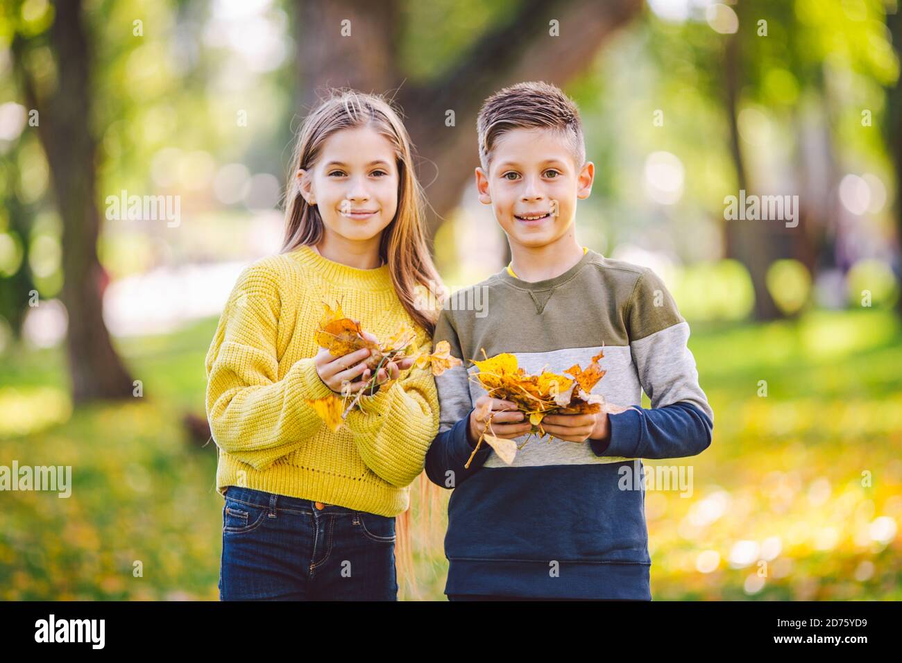 Heureux jumeaux adolescents garçon et fille posant s'embrassant dans le parc d'automne tenant des feuilles jaunes tombées à la main par temps ensoleillé. Thème de la saison d'automne Banque D'Images