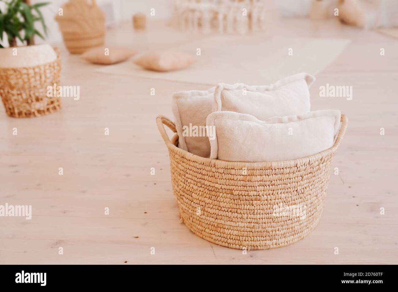 Oreillers doux et légers dans un grand panier en osier sur le sol de la chambre dans un style scandinave minimaliste. Système de rangement confortable et pratique à la maison Banque D'Images