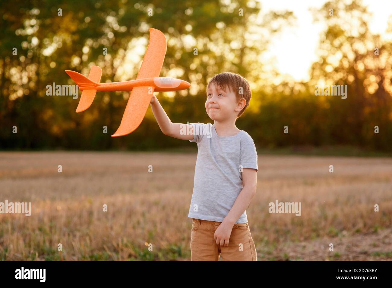Un enfant heureux court avec un avion jouet sur un fond de coucher de soleil sur un champ. Le concept d'une famille heureuse. Rêves d'enfance Banque D'Images