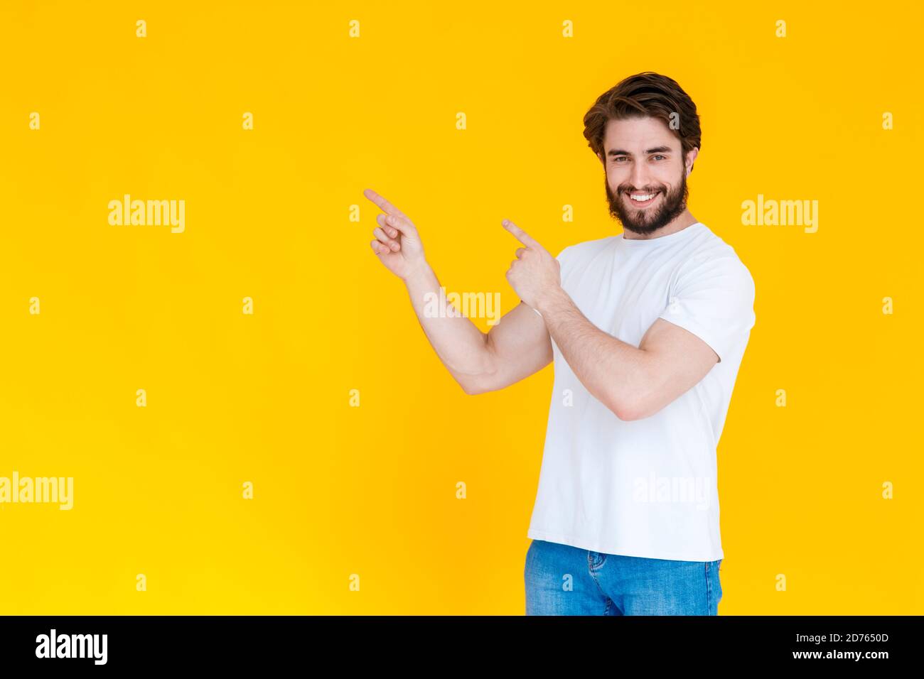 Portrait d'un jeune homme joyeux avec une barbe pointant ses doigts dans la direction de l'espace de copie , isolé sur un fond jaune Banque D'Images