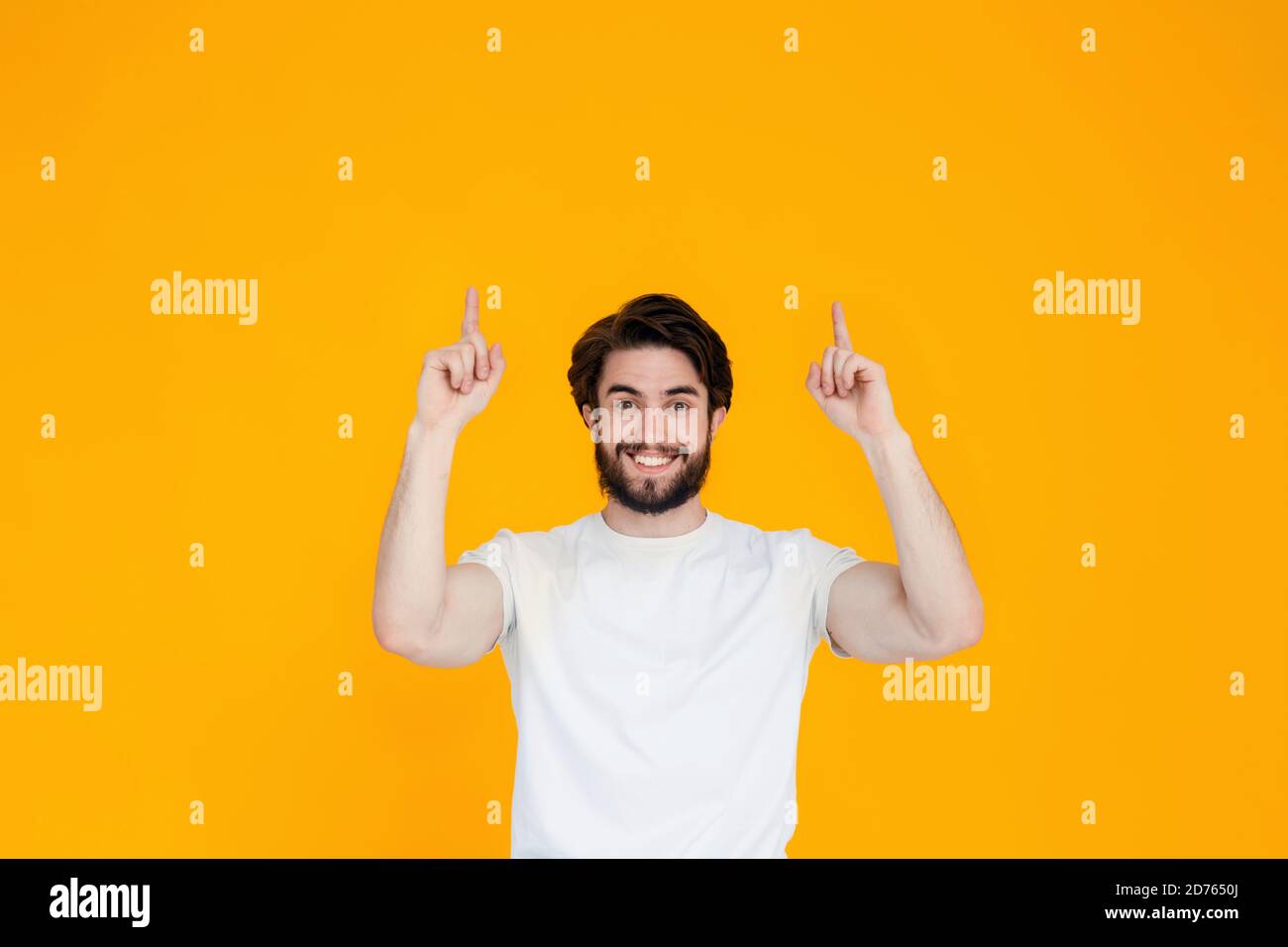 Portrait d'un jeune homme joyeux avec une barbe pointant ses doigts dans la direction de l'espace de copie , isolé sur un fond jaune Banque D'Images