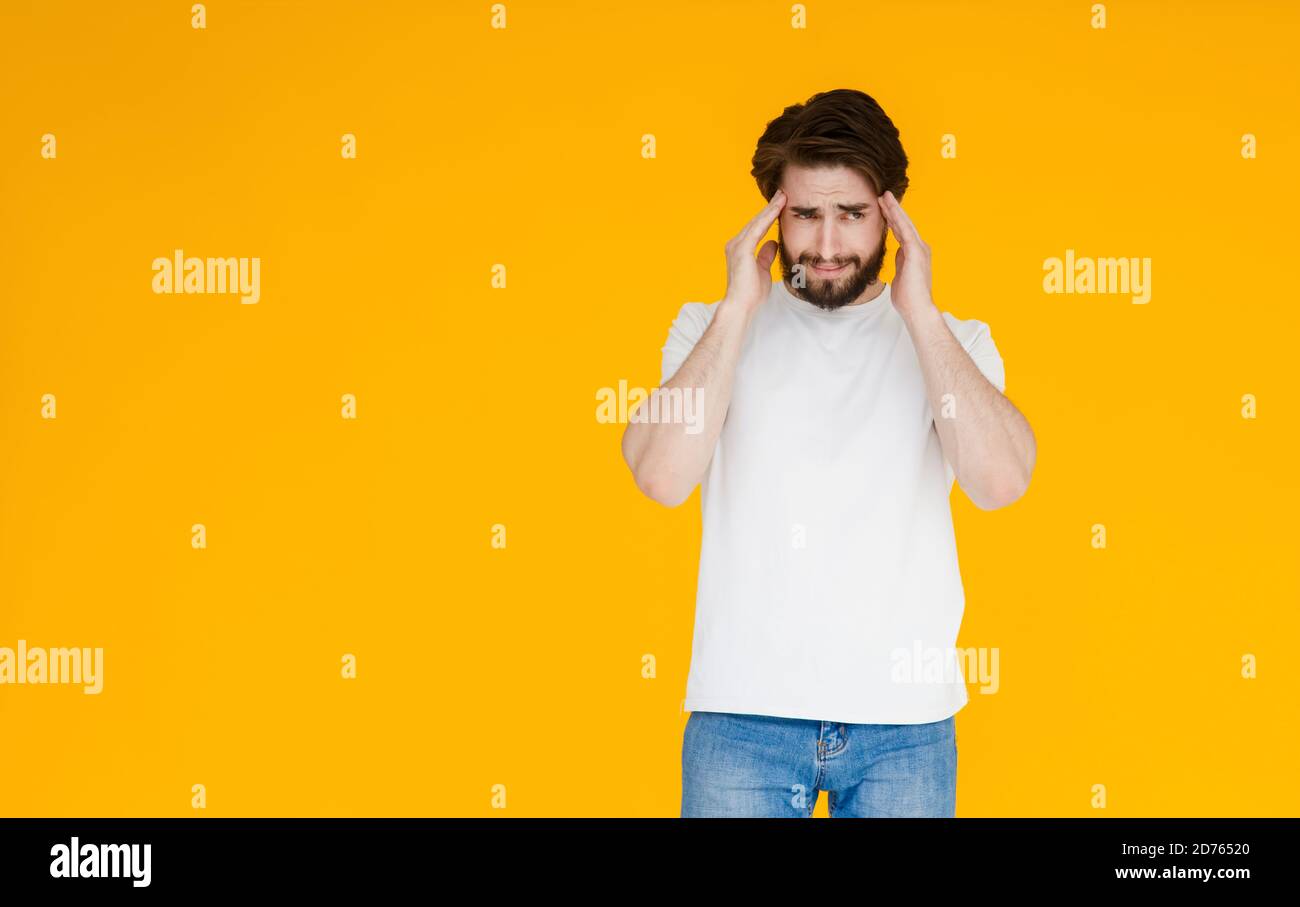 Un jeune homme barbu dans un t-shirt blanc sur fond jaune. Le concept de tension , de mal de tête et de fatigue Banque D'Images