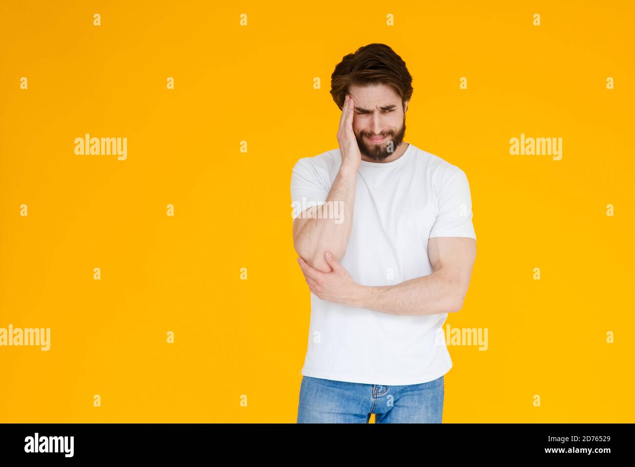 Un jeune homme barbu dans un t-shirt blanc sur fond jaune. Le concept de tension , de mal de tête et de fatigue Banque D'Images